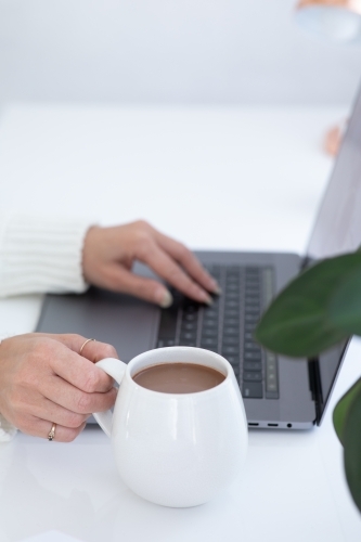 lady's hands typing on laptop with white hug mug in the foreground - Australian Stock Image