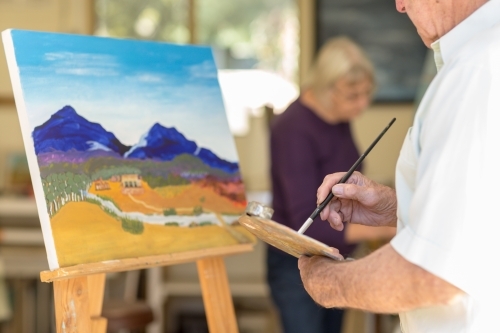 Landscape painting on easel with man holding paintbrush and palette - Australian Stock Image