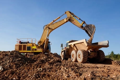 Large digger moving dirt into an earth mover on an industrial building site - Australian Stock Image