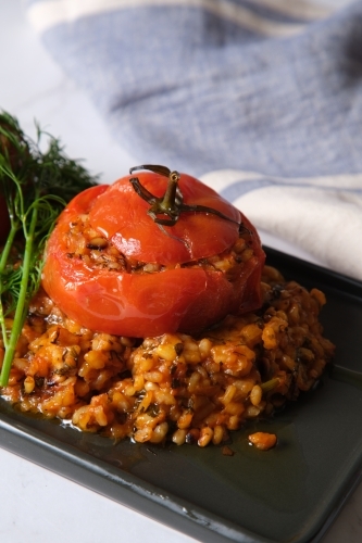 large tomatoes stuffed with rice and green garnish on top - Australian Stock Image