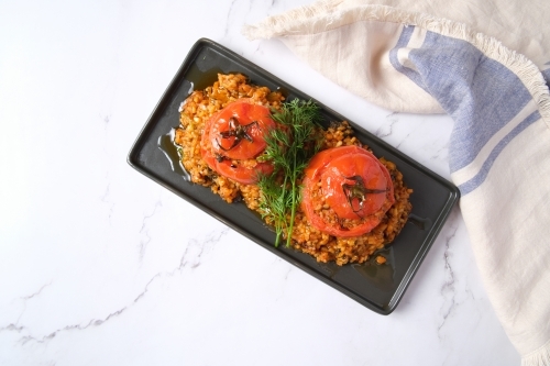 large tomatoes stuffed with rice and green garnish on top - Australian Stock Image
