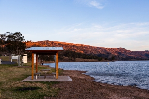 Last light of day on hills behind lakeside picnic shelter and bench - Australian Stock Image