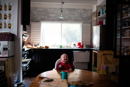 Laughing baby in real messy kitchen - Australian Stock Image