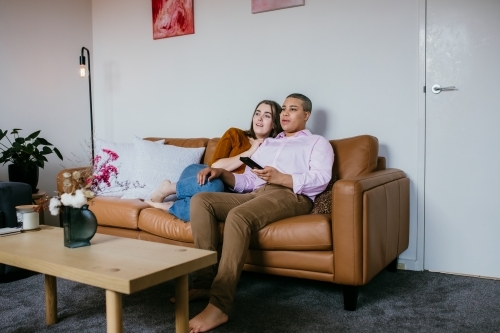 lgbtqi couple sitting on a brown leather couch - Australian Stock Image