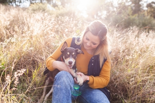 Light flare over young country woman with kelpie pup in grassland - Australian Stock Image