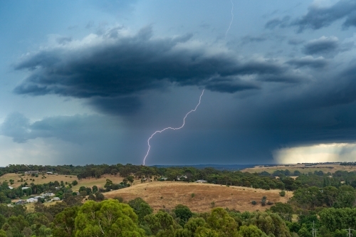 Lightning coming down from a dark storm cloud over a rural town - Australian Stock Image