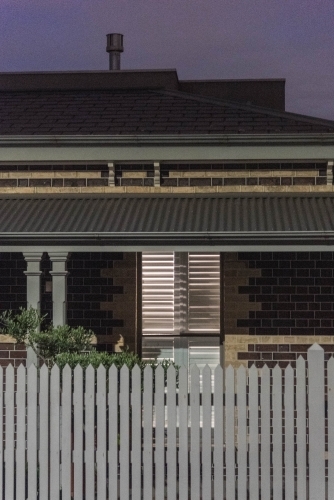 lights on in an inner city heritage home with picket fence at dusk - Australian Stock Image