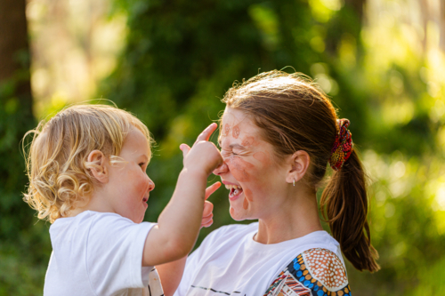 Little aboriginal boy touching ochre face paint on big sister laughing together - Australian Stock Image