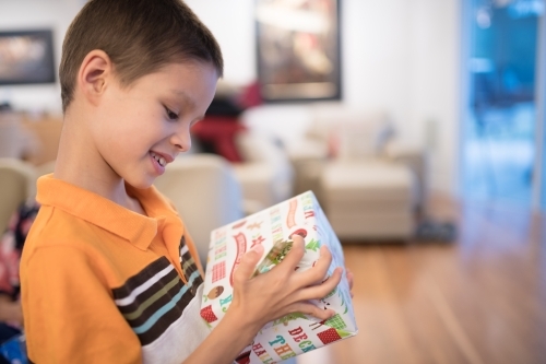 Little boy opening Christmas presents at home - Australian Stock Image