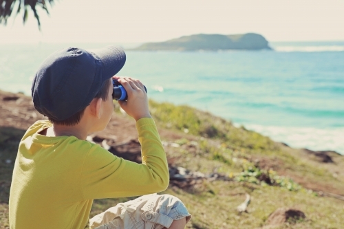 Little boy using binoculars looking over oceans