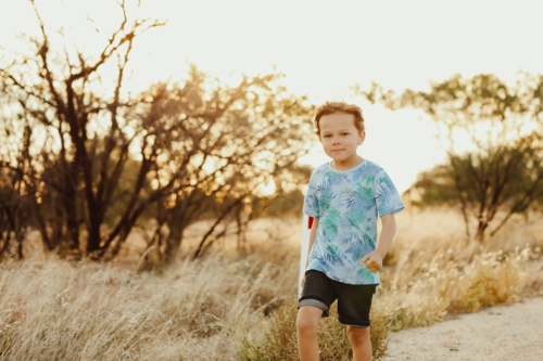 Little boy walking along rural gravel road in golden afternoon light - Australian Stock Image