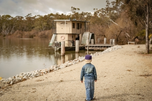 Little boy walking towards houseboat moored along the Murray River - Australian Stock Image