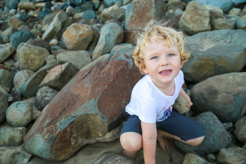 Little curly haired blond boy playing on rocks by the beach - Australian Stock Image