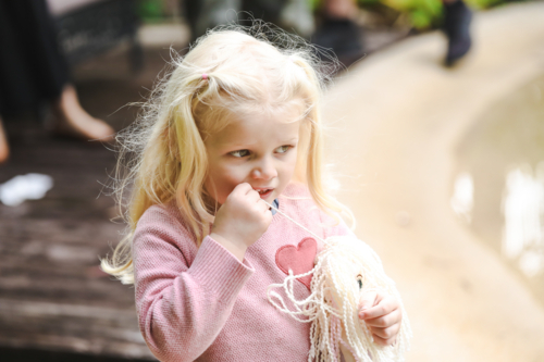 Little girl chewing on hair of doll looking thoughtful - Australian Stock Image