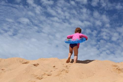 Little girl climbing a sanddune with an inflatable ring