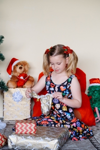 Little girl in an emoji dress opening a Christmas present - Australian Stock Image