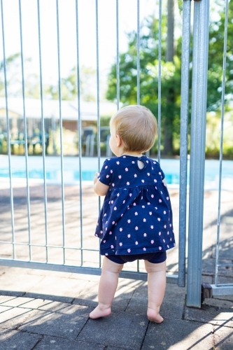 Little girl standing at a pool gate in summer - Australian Stock Image