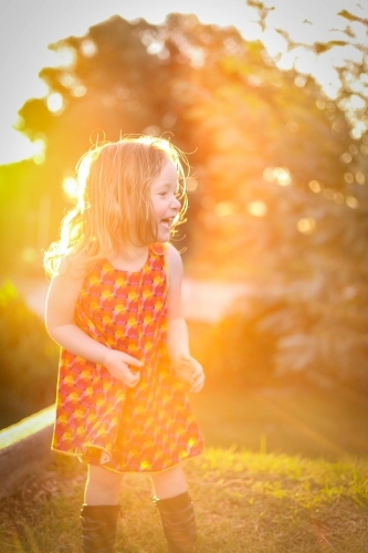 Little girl wearing red dress exploring garden flooded in golden afternoon light - Australian Stock Image