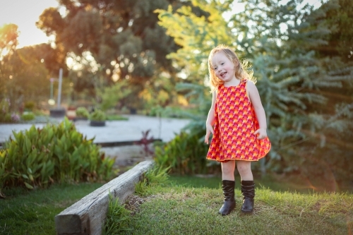 Little girl wearing red dress exploring lush green garden - Australian Stock Image