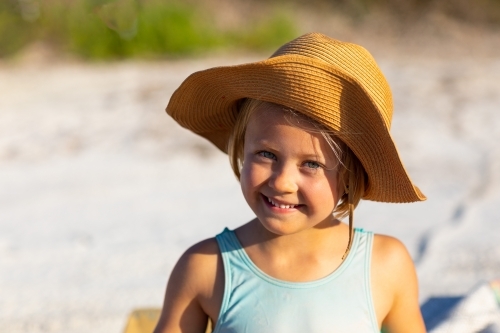 little girl wearing straw hat under the sun at the beach - Australian Stock Image