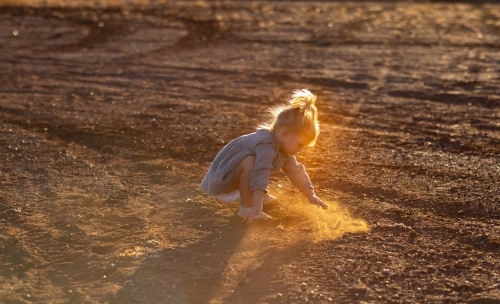 little kid playing in the dirt with backlight highlighting dust