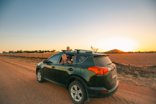 Little kids hanging out window and sunroof of small vehicle on dirt road - Australian Stock Image