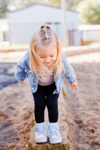 Little preschool girl balancing along wall in kindergarten yard - Australian Stock Image