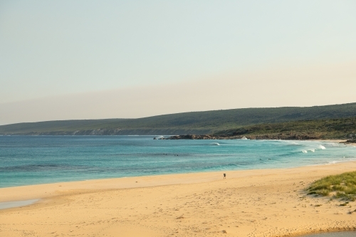 Loan hiker walking on beach with surfers in water - Australian Stock Image