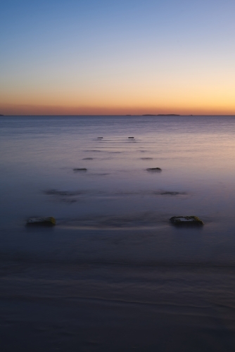 Long exposure of a peaceful ocean at dusk with stumps of an old jetty.