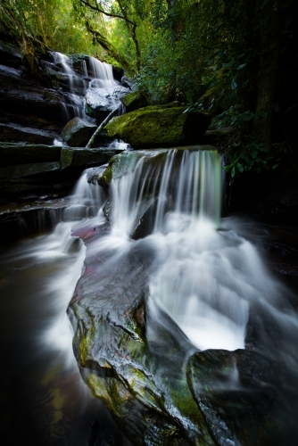 Long exposure of mossy waterfall in dark green forest - Australian Stock Image