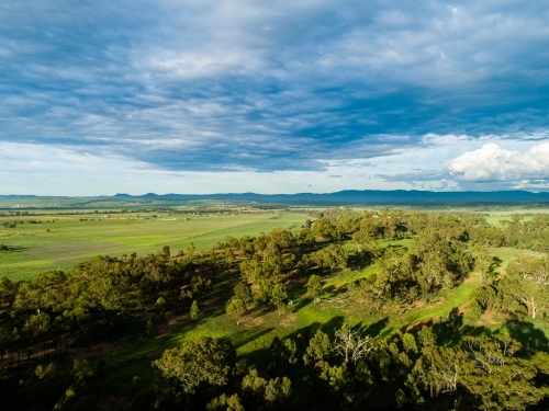 Long shadows over paddock with green grass and rain clouds - Australian Stock Image