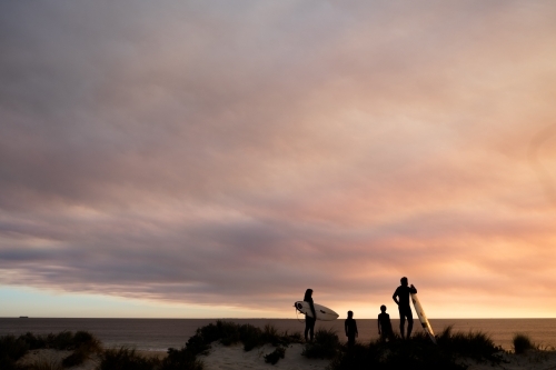 Long shot silhouette of family of four overlooking coastal seascape with moody sunset - Australian Stock Image
