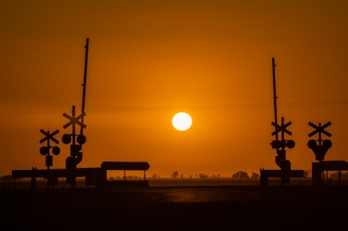 Looking at the sun rising directly behind a railway line crossing. - Australian Stock Image