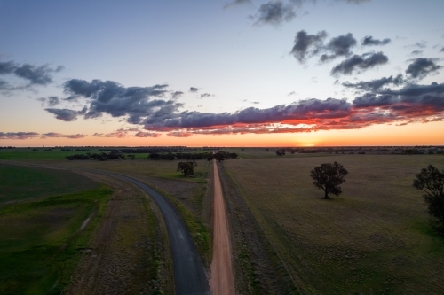 Looking down along the dirt road with the sun setting in the distance. - Australian Stock Image