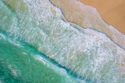 Looking down at the surf coming onto the sand on a beach - Australian Stock Image