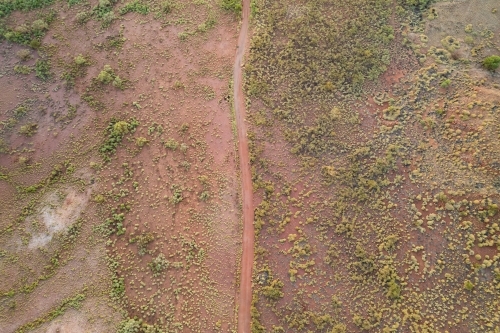 Looking down on a red earth dirt track speckled with green bushes over the land. - Australian Stock Image
