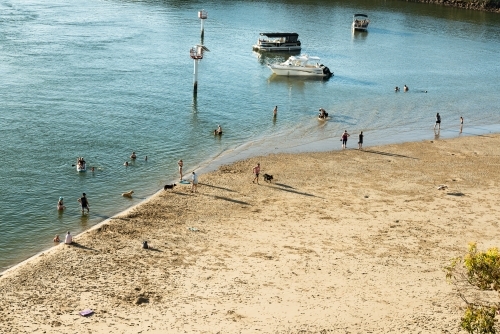 Looking down on people at a beach on  a rivers edge with boats and dogs - Australian Stock Image