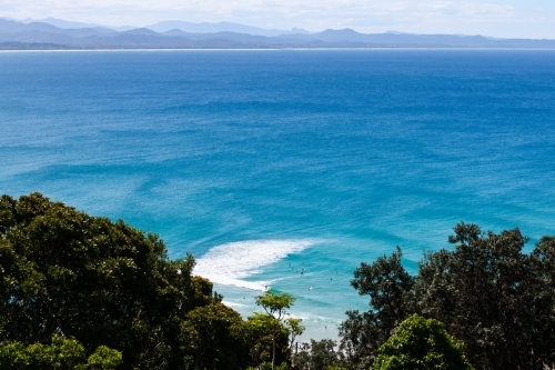 Looking down on surfers in blue ocean with patterns in water and distant mountains - Australian Stock Image