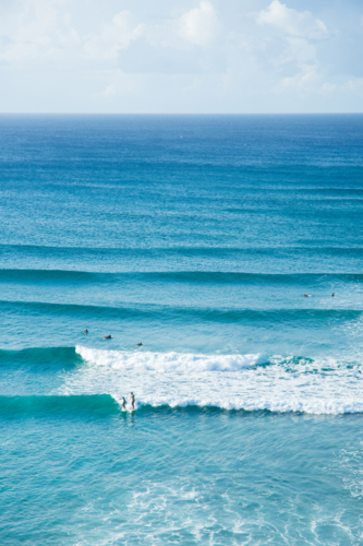 Lots of blue waves rolling in with people surfing at Byron Bay - Australian Stock Image