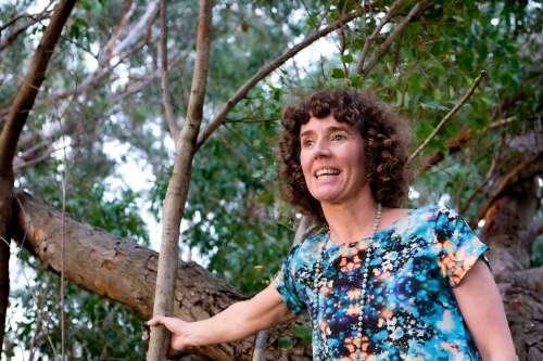 Low angle of Mature woman holding onto trunk of tree looking out - Australian Stock Image