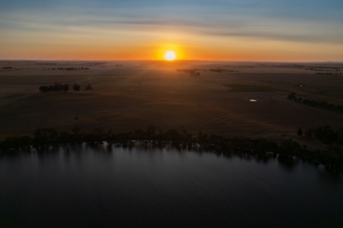 Low sun over landscape with lake in foreground - Australian Stock Image