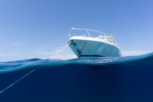 Luxury boat sitting on anchor floating in deep blue water with blue sunny skies in background - Australian Stock Image