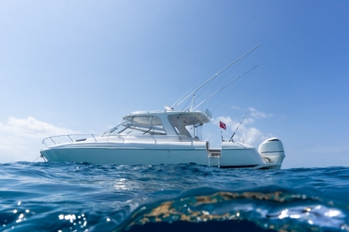 Luxury boat with dive flag, floating in deep blue water with blue sunny skies in background - Australian Stock Image