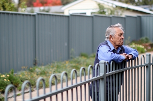 Male Aboriginal elder leaning against fence looking away from camera - Australian Stock Image