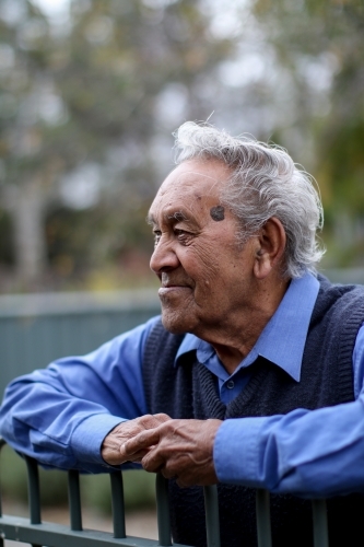 Male Aboriginal elder smiling and leaning against fence - Australian Stock Image