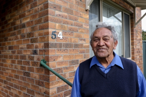 Male Aboriginal elder standing in front of his home