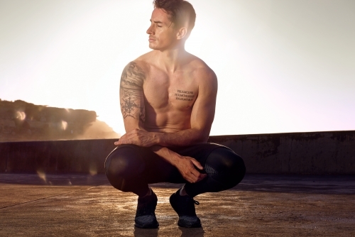 Male doing exercise in morning beside ocean - Australian Stock Image