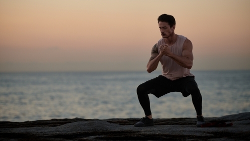 Male doing stretch exercise beside ocean - Australian Stock Image