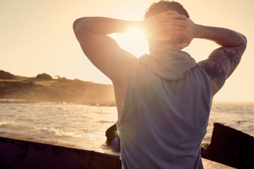 Male doing stretch exercise beside ocean - Australian Stock Image