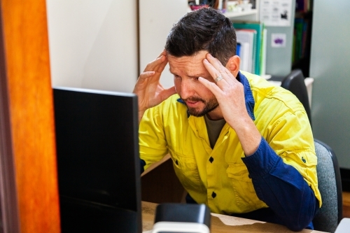 Male tradie at home office desk feeling overwhelmed and exhausted - Australian Stock Image